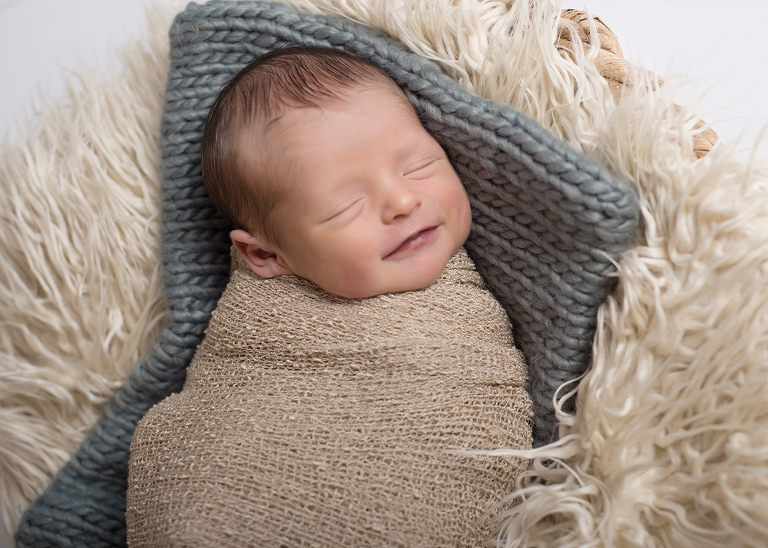 smiling newborn photo on beige fur and gray blanket