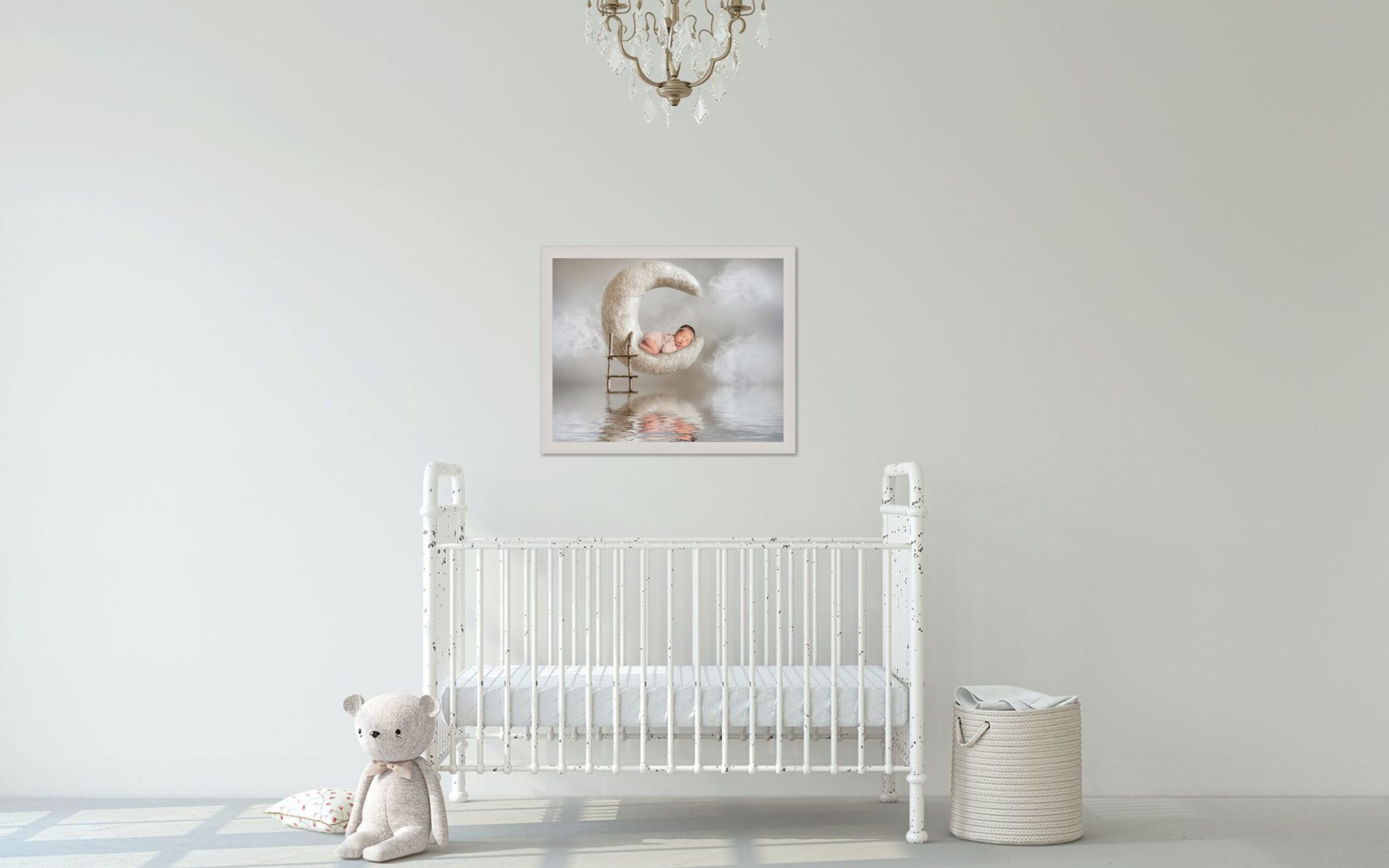 White room with a vintage white metal crib and gold chandelier with a framed picture of a baby girl on a moon prop