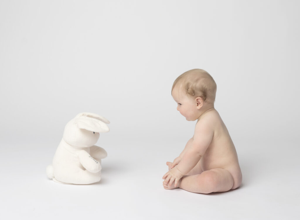 naked baby boy sitting looking at his stuffed bunny