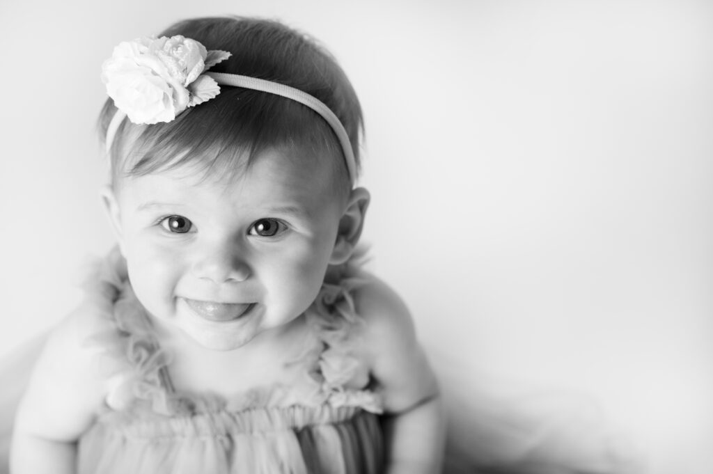 black and white image of baby girl looking up at the camera sticking her tongue out