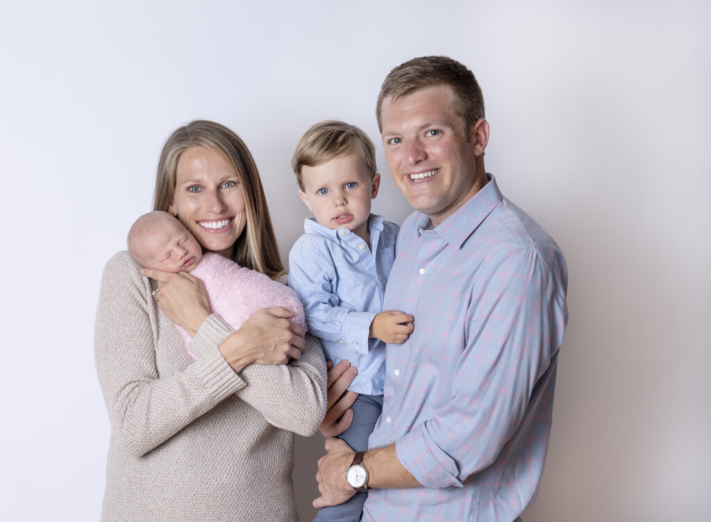 Family of four - mom is holding her newborn daughter and dad is holding his toddler son.