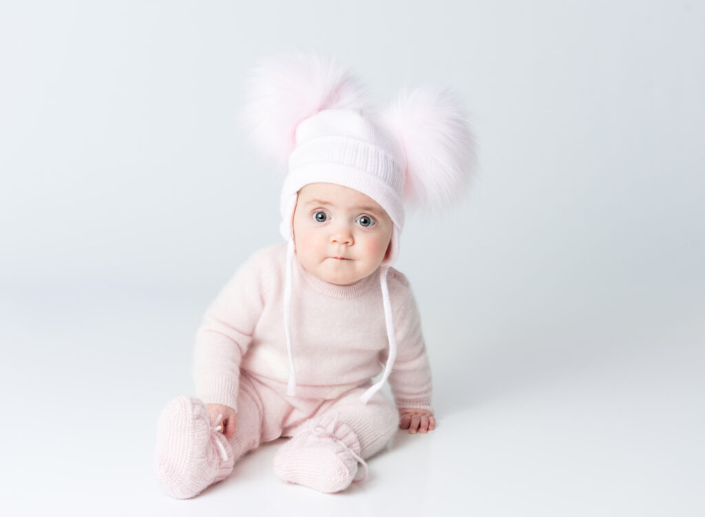 baby girl in fuzzy pink outfit and hat with pom-poms