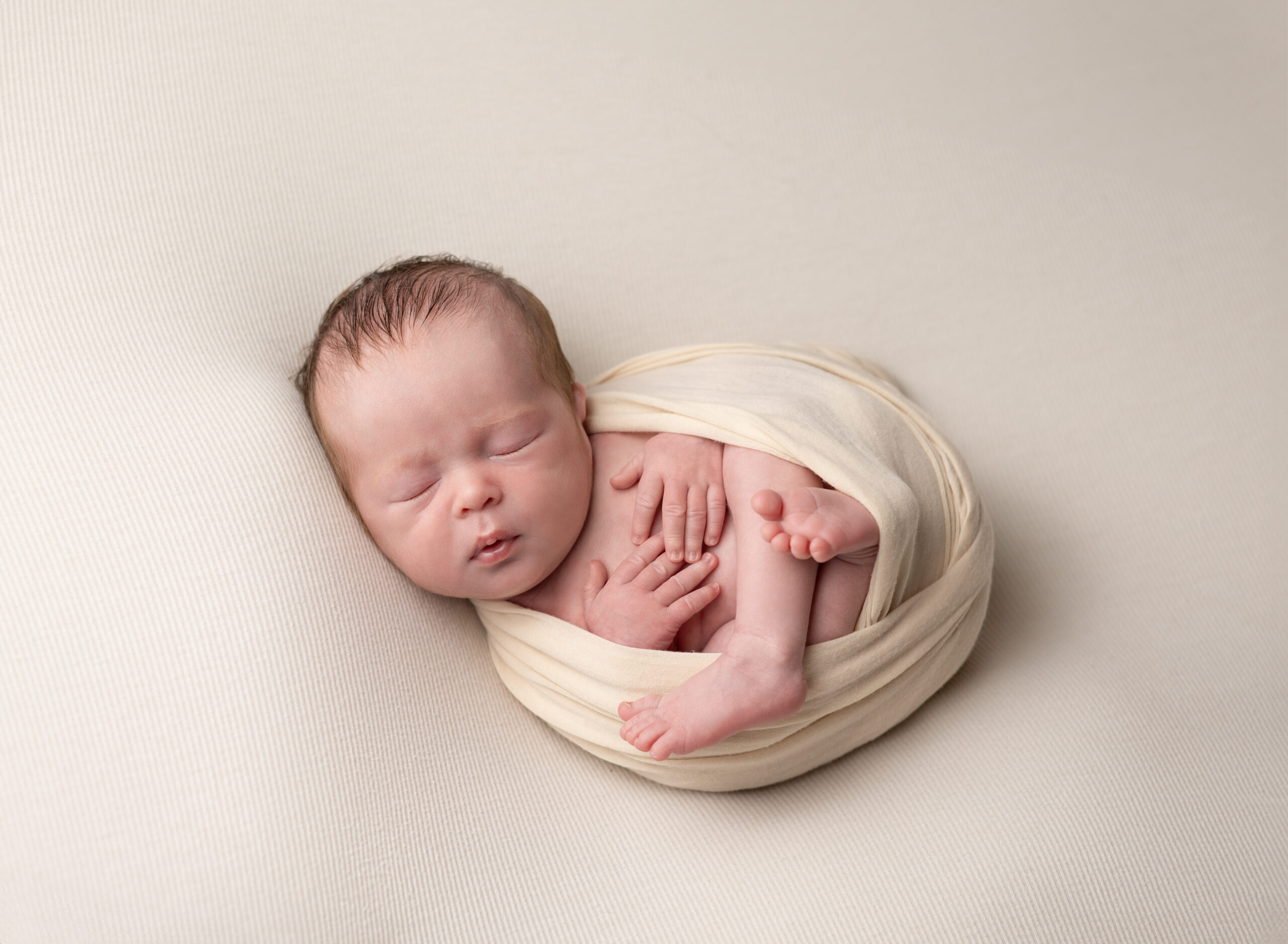 newborn boy swaddled in cream wrap