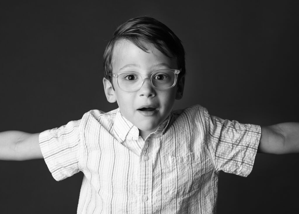 black and white image of young boy wearing glasses with his arms outstretched