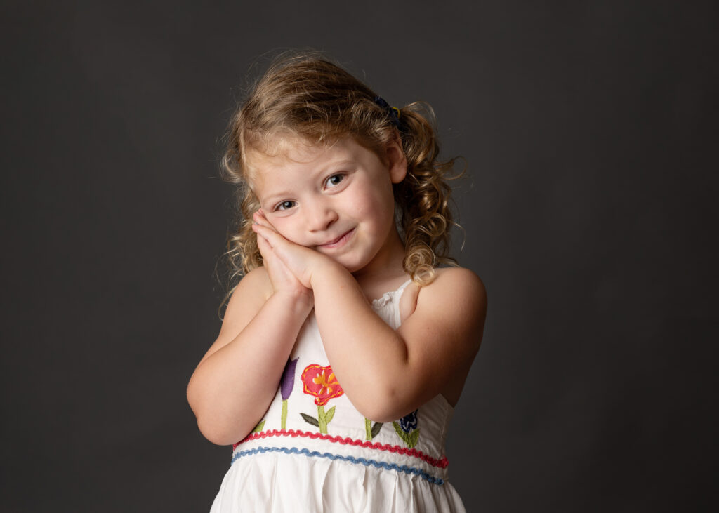 young girl with curly hair holding her hands up on the side of her face with prayer hands