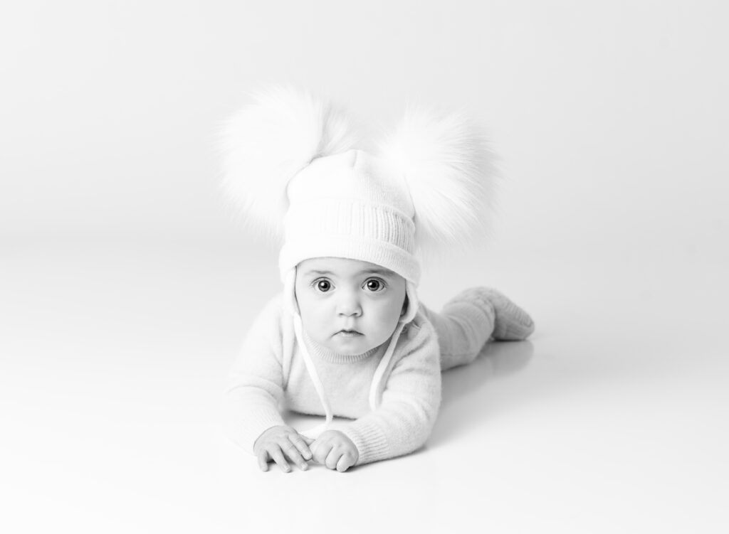 chicago baby laying on her tummy with a cute knit footed outfit and a knit hat with big pom-poms in black and white