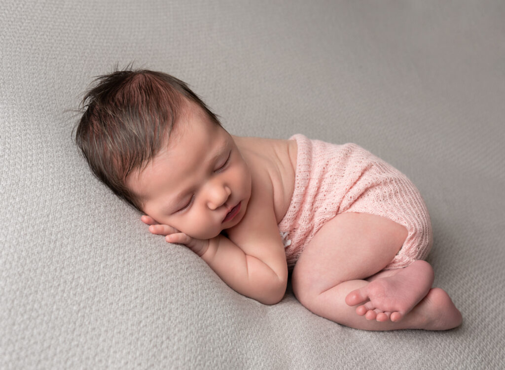newborn baby girl in pink knit jumper curled up for professional newborn photos