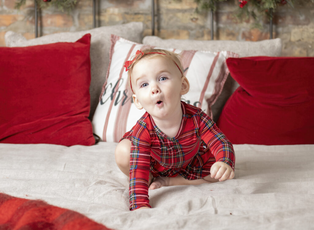 toddler girl wearing holiday pajamas crawling on a bed