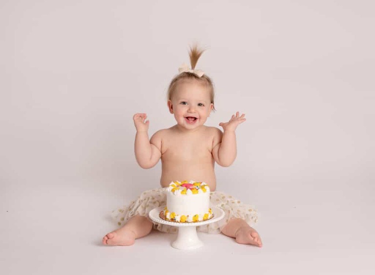 Annie smiling before digging in to her Sweet Mandy B's cake during her 1st birthday cake smash session!